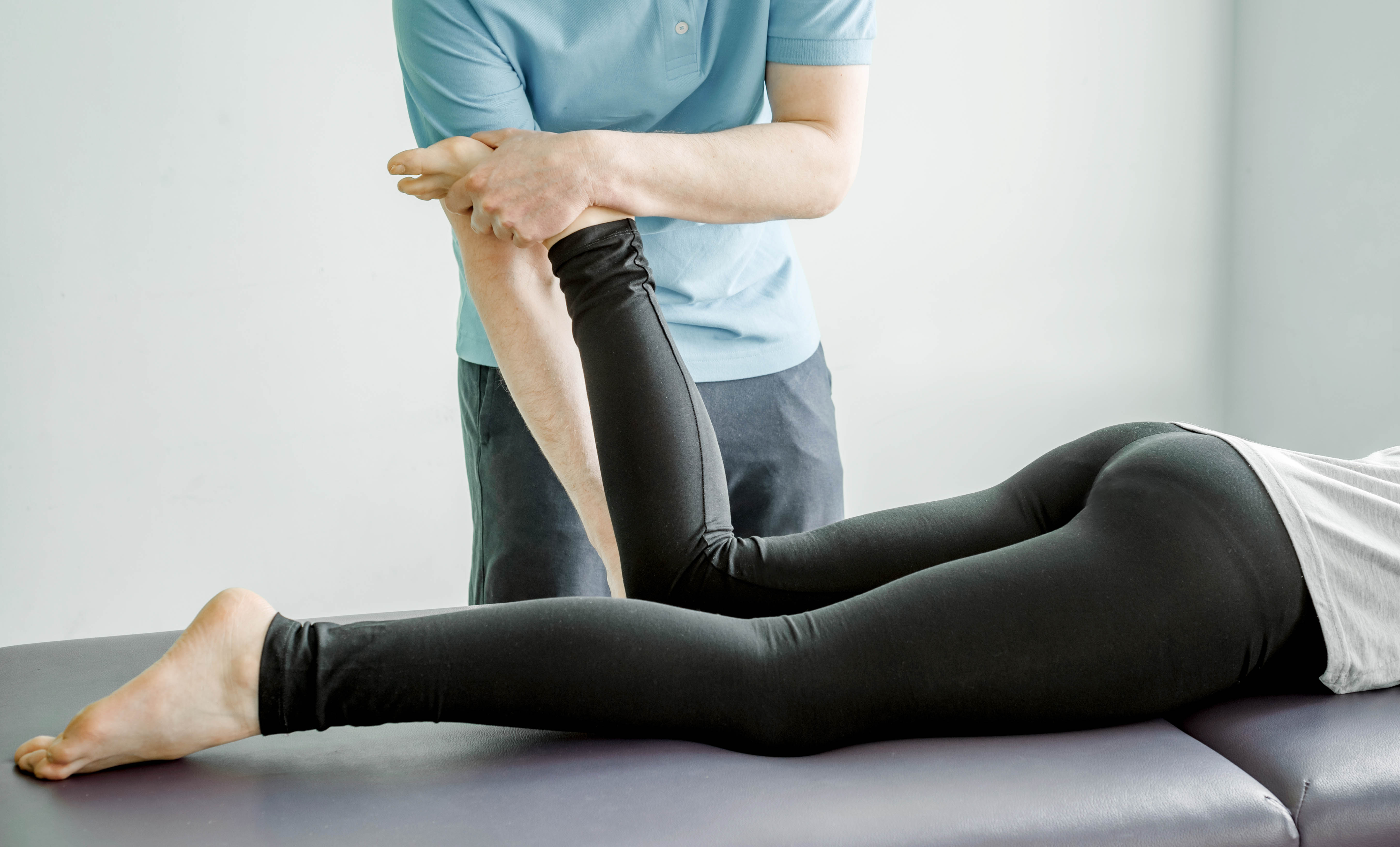 Young female patient lays face down on the table, practitioner is doing fascial stretch therapy on her lower leg and knee Young female patient lays face down on the table, practitioner is doing fascial stretch therapy on her lower leg and knee